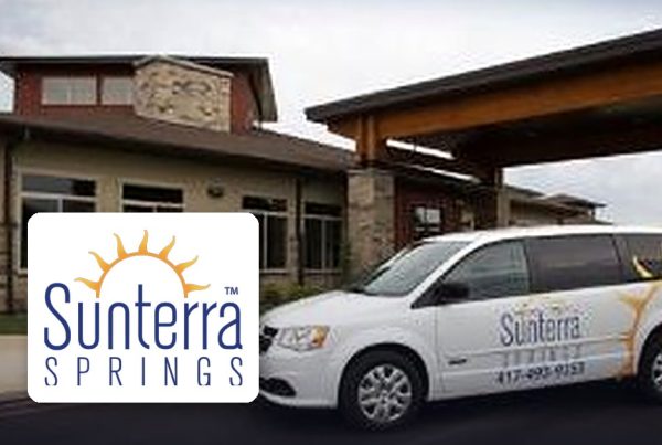 Sunterra Springs facility with a branded white van parked in front and the Sunterra logo visible on the vehicle and logo overlay.