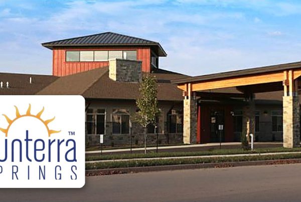 Exterior view of the Sunterra Springs facility with a modern entrance; logo overlay in the bottom-left corner.